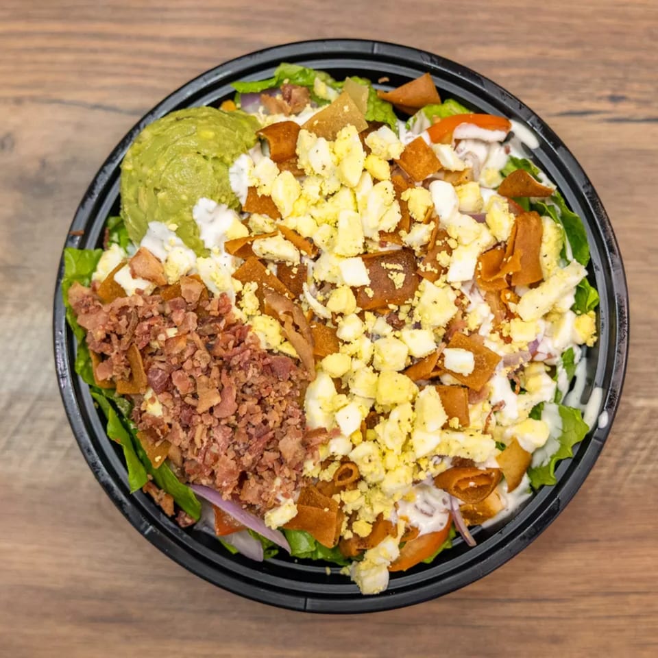 Overhead view of a salad with guacamole, bacon bits, chopped eggs, and tortilla strips.