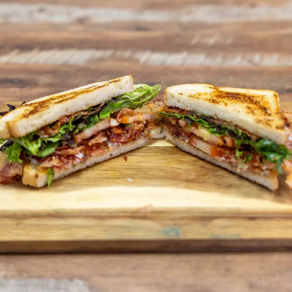 A toasted club sandwich, cut in half, revealing layers of bacon, lettuce, and tomato on a wooden board.