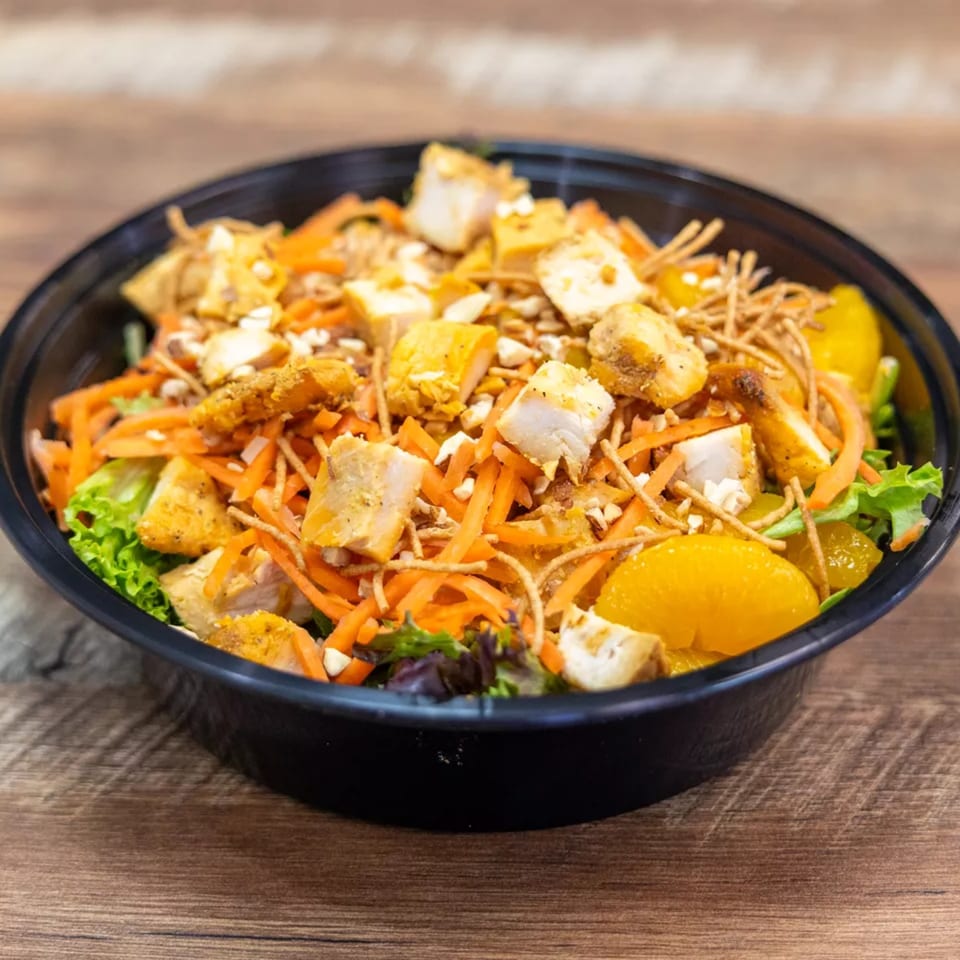 A vibrant salad with chicken, shredded carrots, mandarin oranges, and crispy noodles in a black bowl.