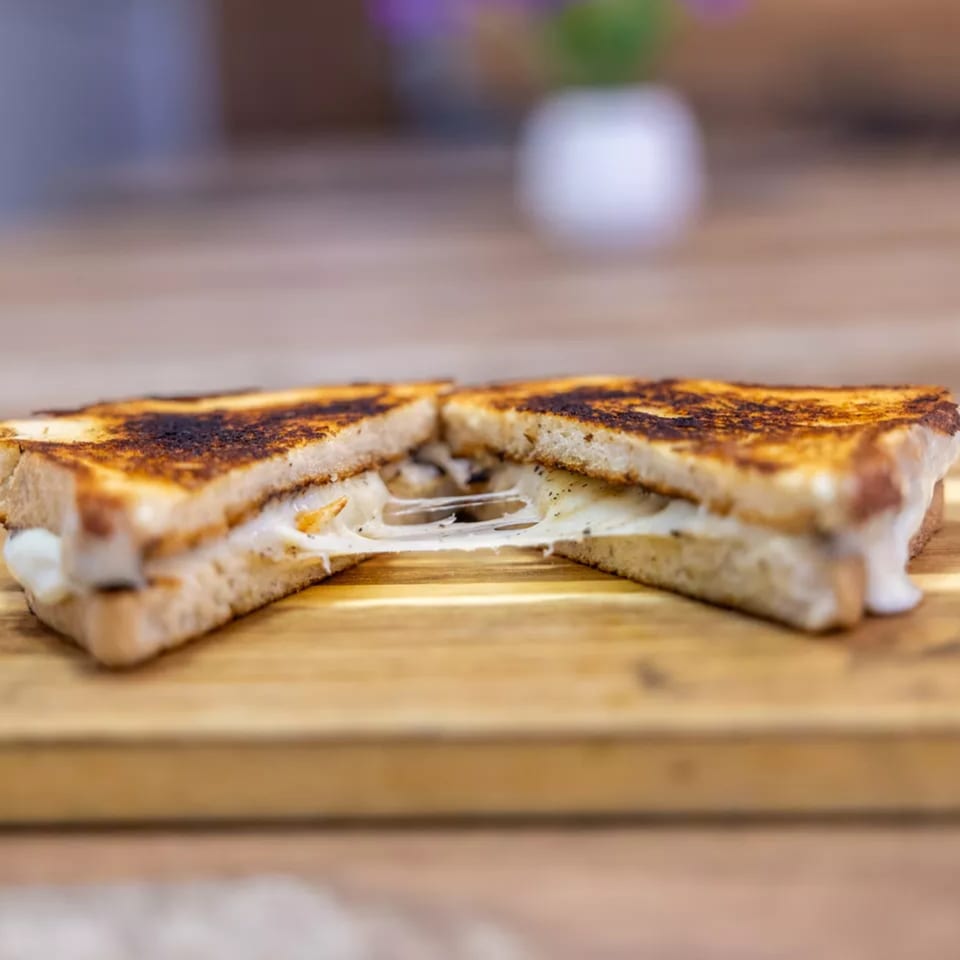 A grilled cheese sandwich, cut in half, with melted cheese stretching between the halves.
