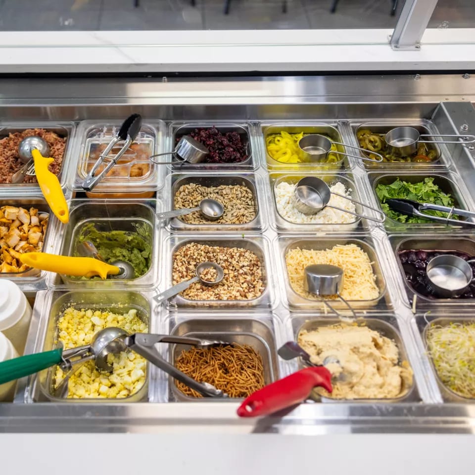 Overhead view of a salad bar with various toppings in metal and plastic containers.