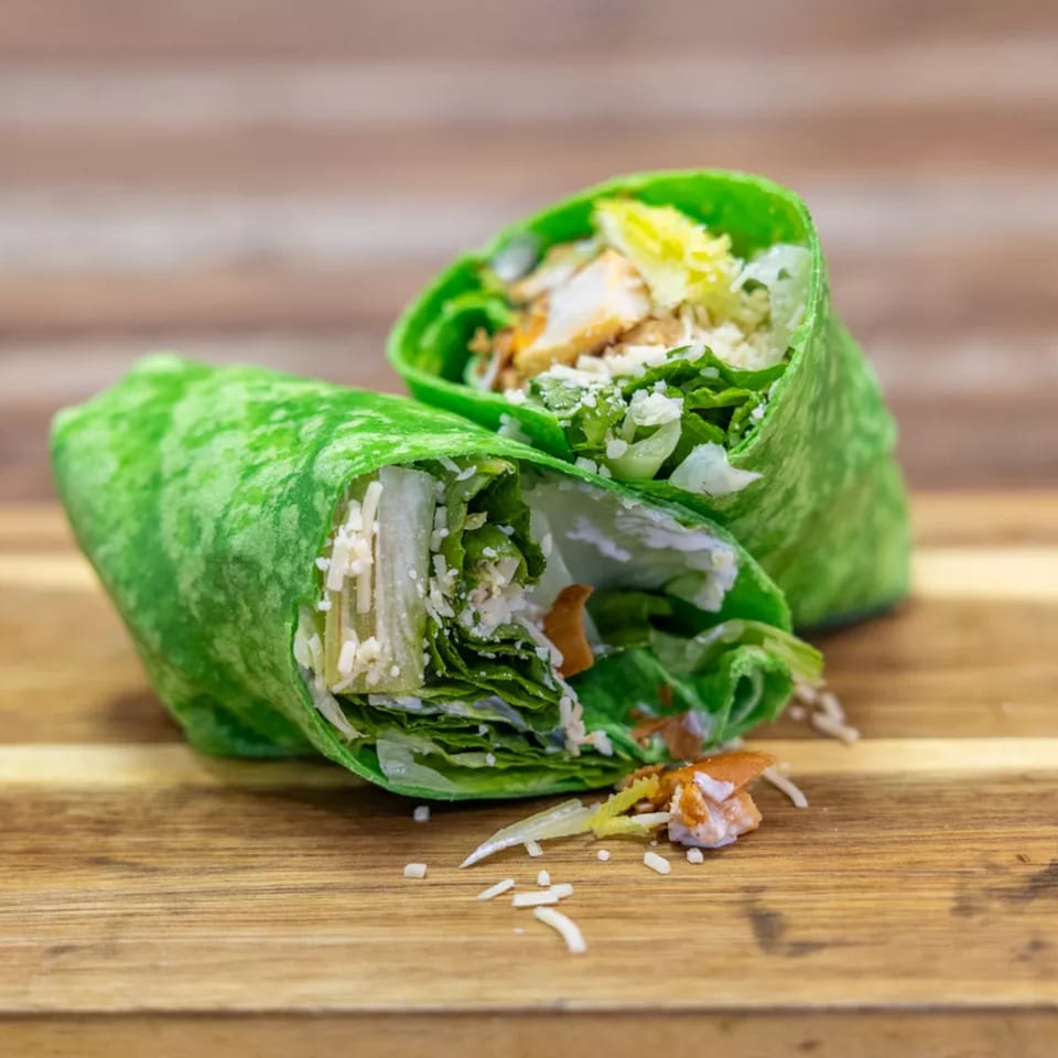Two vibrant green wraps filled with chicken, lettuce, and cheese, on a wooden cutting board.
